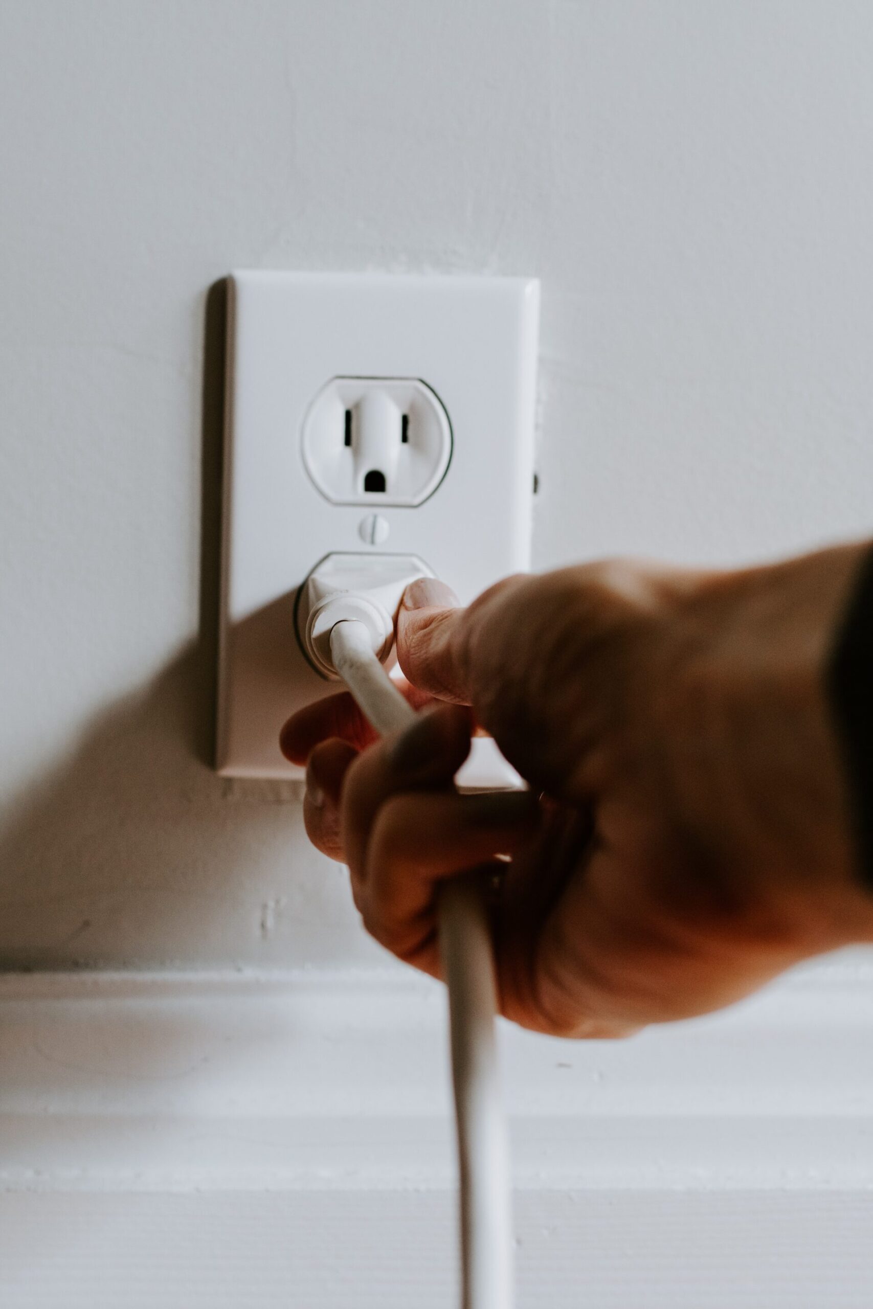 A hand plugging a cord into an electrical outlet.